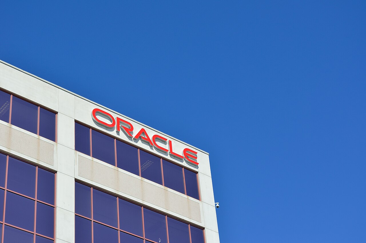 The red Oracle logo on the side of a modern office building against a clear blue sky.