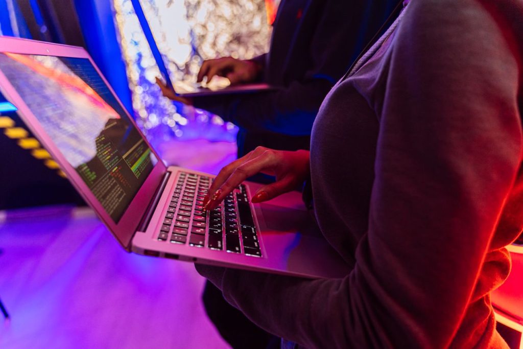 A close-up view of hands typing on a laptop displaying code and user authentication workflows, representing identity and age verification data architecture.