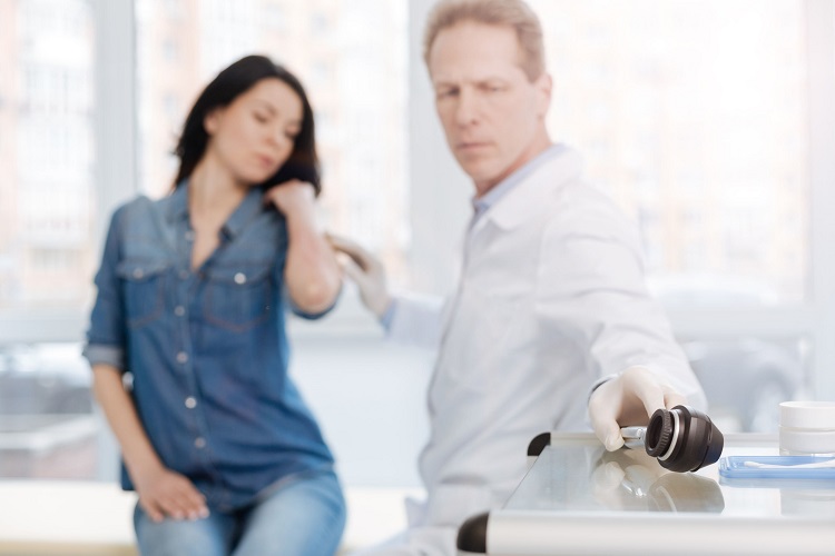 Doctor reaching for a dermascope to examine a patient's skin lesion